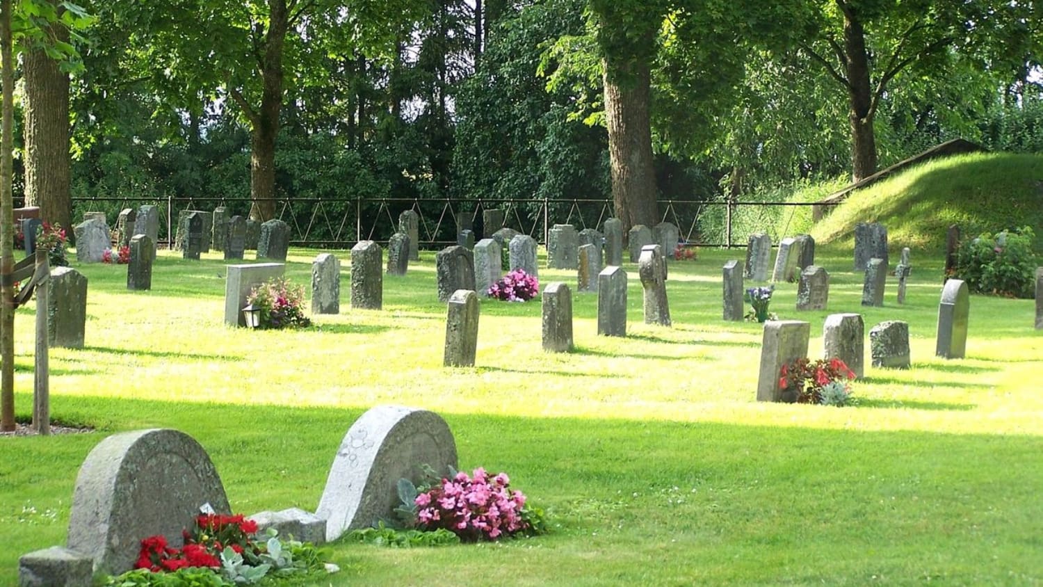 A cemetery with many headstones and flowers on the ground.